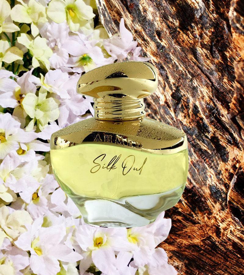 Luxury Silk Oud perfume bottle with golden cap, surrounded by white flowers and rustic wood
