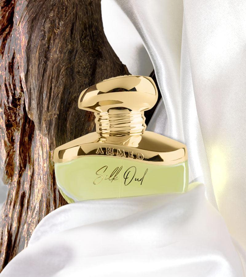 Luxury Silk Oud perfume bottle with gold cap, nestled in white silk beside textured wood