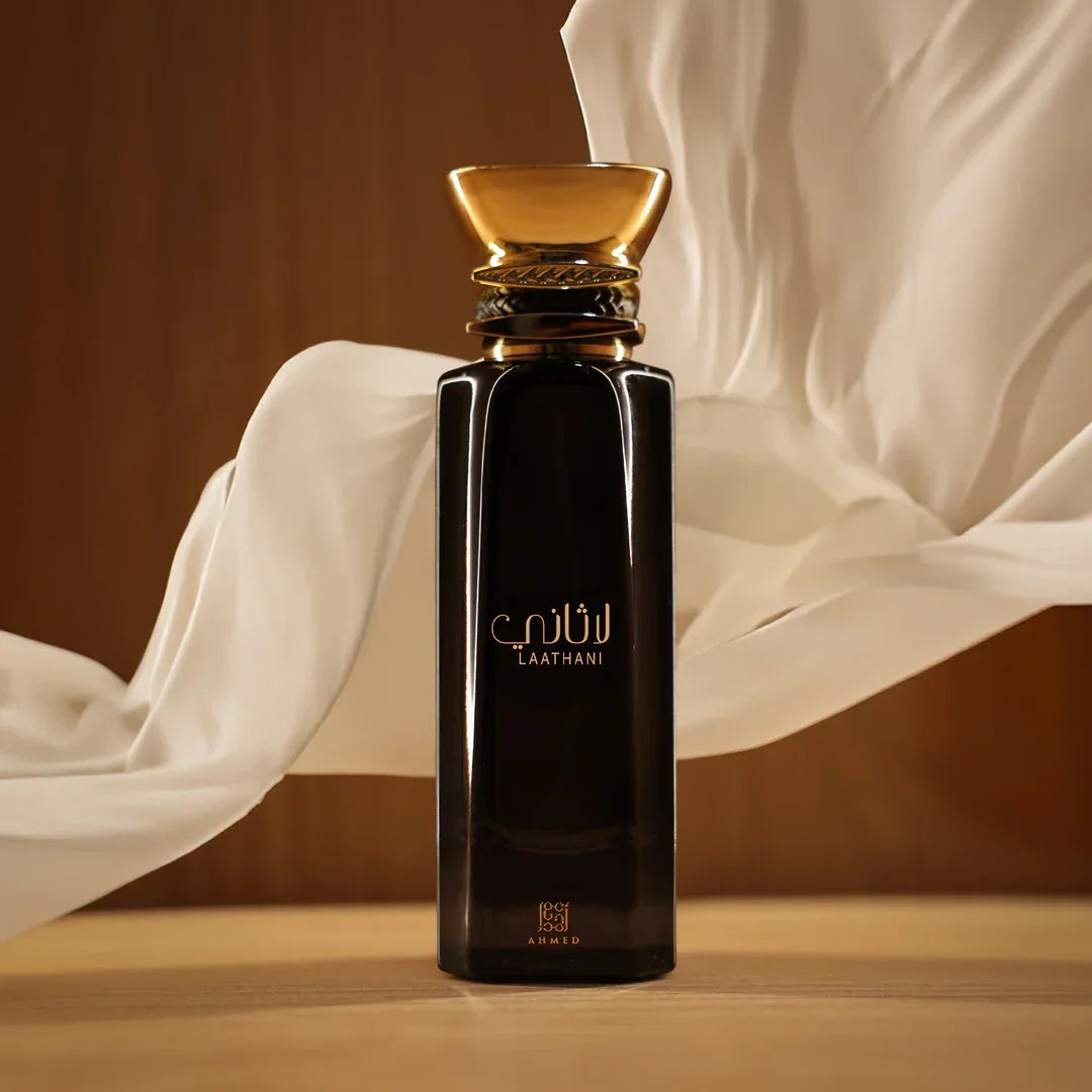 Elegant Laathani perfume bottle with gold cap on a wooden surface, flowing white fabric backdrop